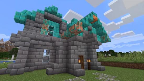 Construction en cuivre Minecraft : Un bâtiment en briques de pierre, surmonté d'un toit de blocs de cuivre de différents degrés d'oxydation.