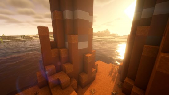 Minecraft shaders - the sun sets through the buttes of a badlands biomes, over realistic looking water, with BSL shaders installed