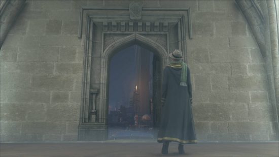 Hogwarts Legacy Room of Requirement - the door to the Room of Requirement appears on a blank wall near the player character, who is dressed in Hufflepuff robes, a scarf, and a trilby hat.