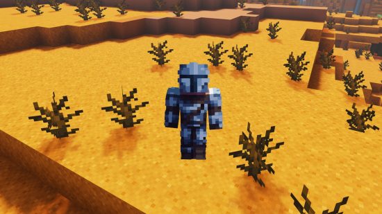 A player dressed in a Mandalorian Minecraft skin stands on sun baked red sand, surrounded by dead bushes.
