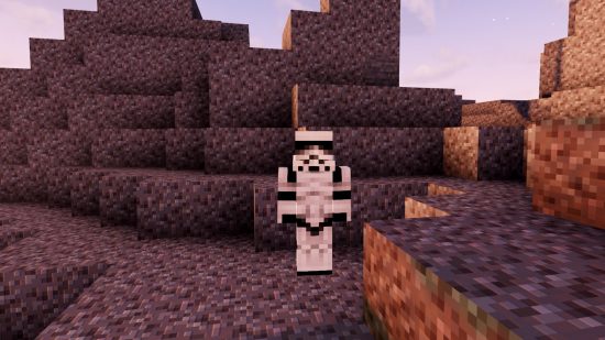 A player in a Stormtrooper Minecraft skin stands in a grey, barren landscape full of gravel, as the sun sets, casting shadows.