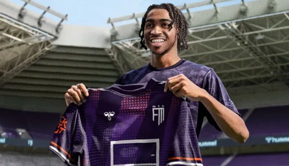 A young Black male smiling as he proudly holds up a football shirt for his new club