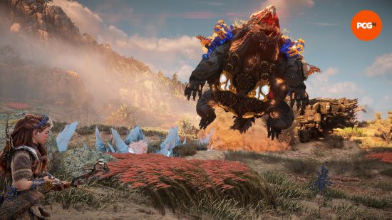 Horizon Forbidden West: a warrior kneels in tall grass as a giant robot dinosaur leaps nearby.